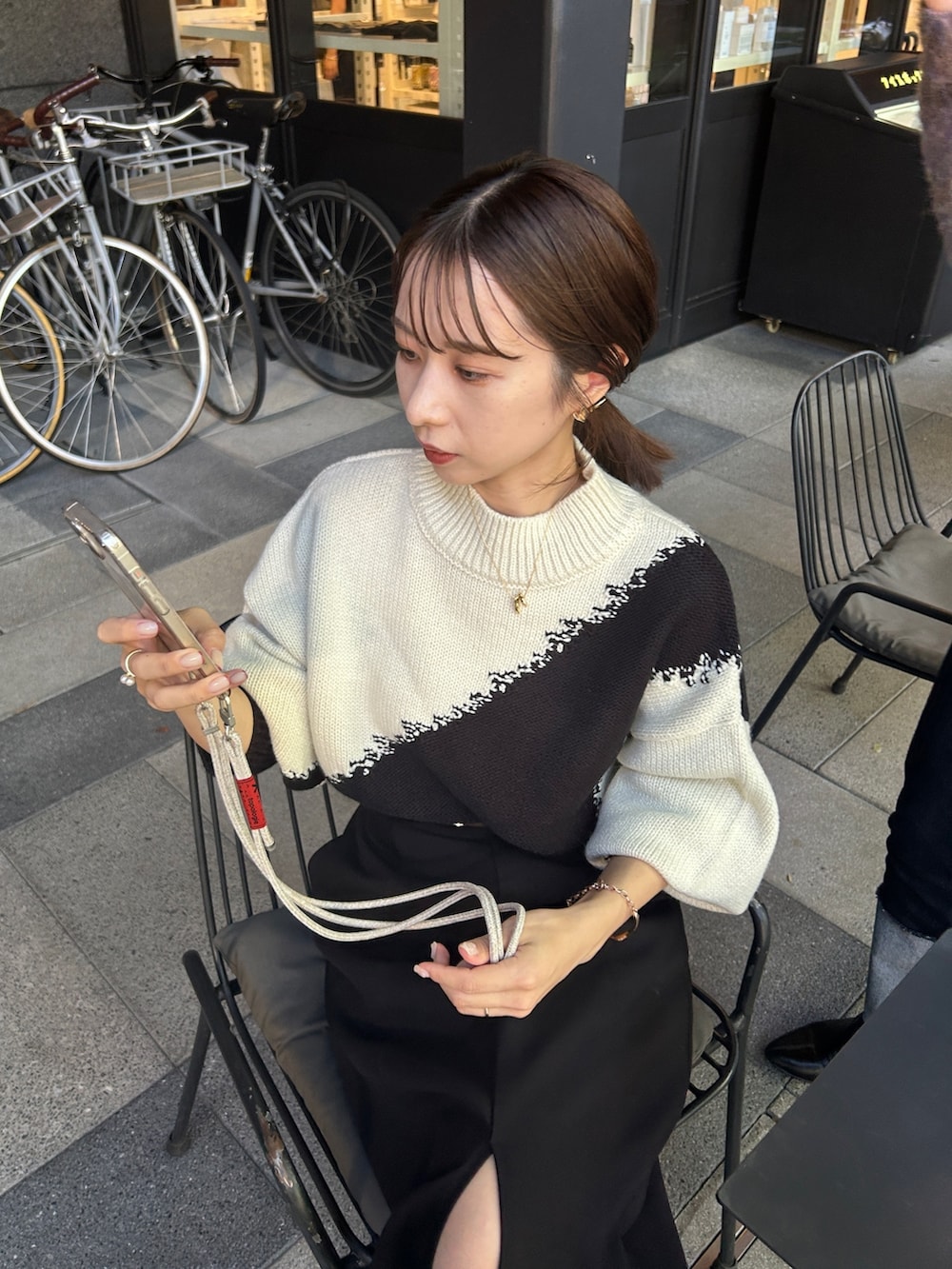 ブラック系のスカート、ホワイト系のニット/セーター、ブラック系のショルダーバッグを着用したレディースの秋コーディネートの3枚目の写真