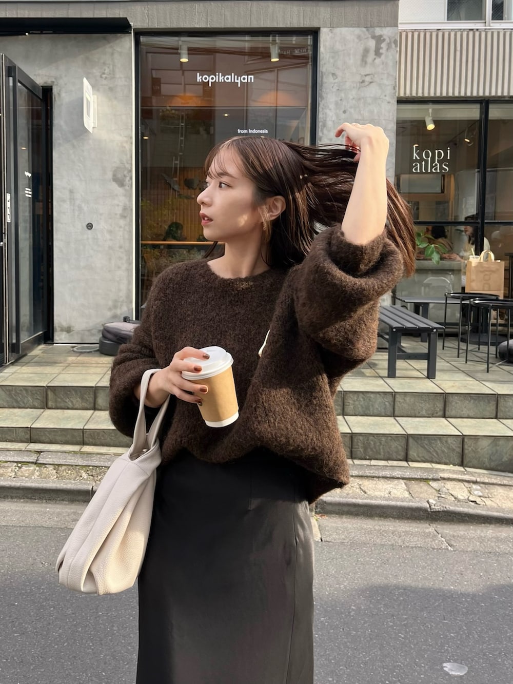 ブラック系のスカート、ブラウン系のニット/セーター、ホワイト系のハンドバッグを着用したレディースの秋コーディネートの3枚目の写真