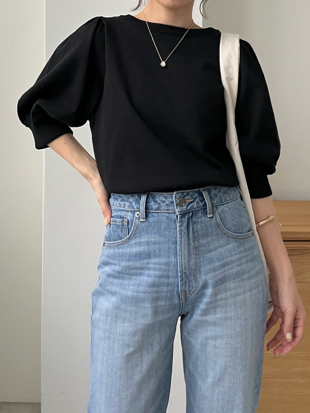 ブルー系のデニムパンツ、ホワイト系のバッグ、ブラック系のニット/セーターを着用したレディースの春コーディネートの4枚目の写真