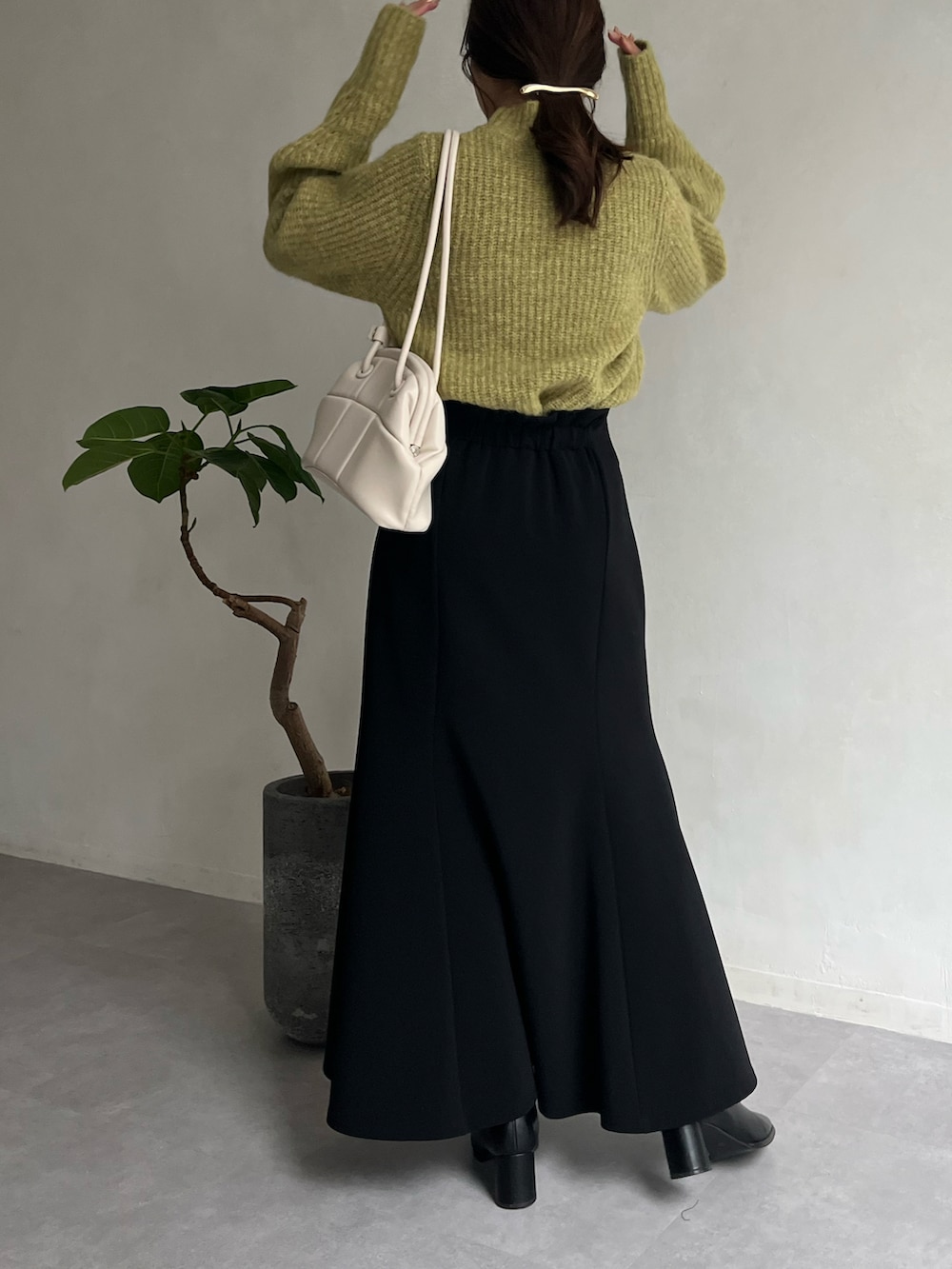 グリーン系のニット/セーター、ブラック系のスカート、ブラック系のブーツを着用したレディースの冬コーディネートの2枚目の写真