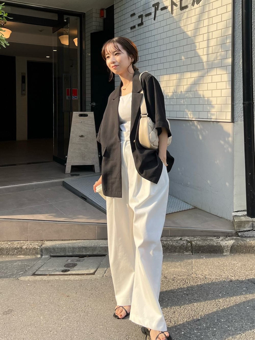 ブラック系のテーラードジャケット、ホワイト系のバッグ、ホワイト系のキャミソールを着用したレディースの春コーディネートの4枚目の写真