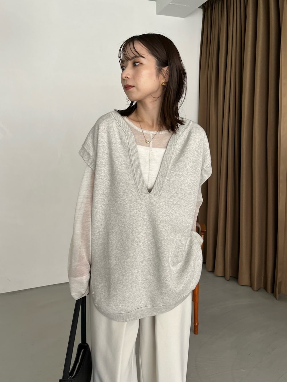 グレー系のベスト、ホワイト系のニット/セーター、ブラック系のパンプスを着用したレディースの秋コーディネートの3枚目の写真