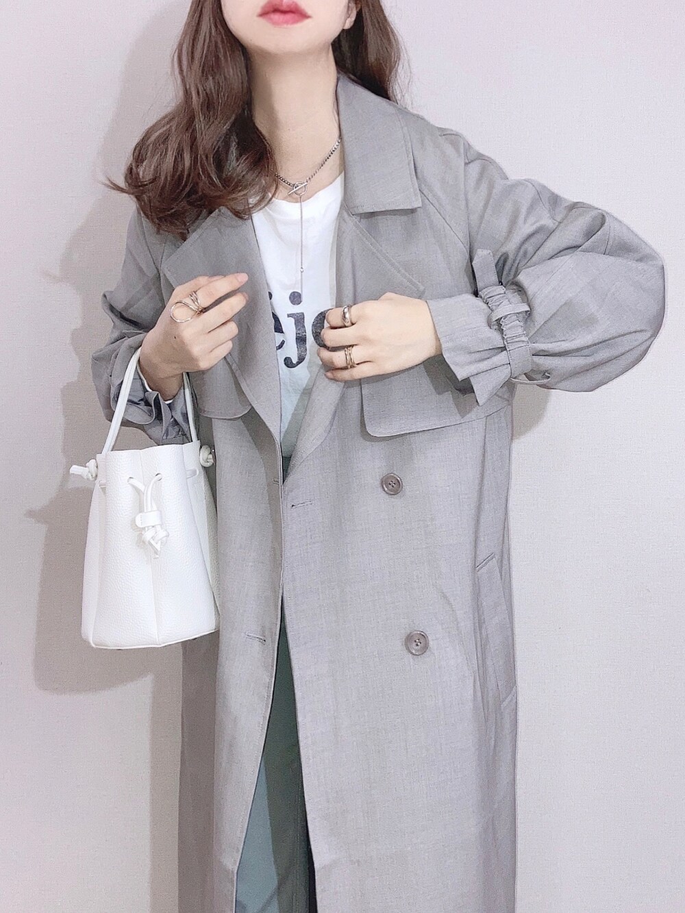 グレー系のトレンチコート、ホワイト系のTシャツ/カットソー、グリーン系のパンツを着用したレディースの冬コーディネートの2枚目の写真