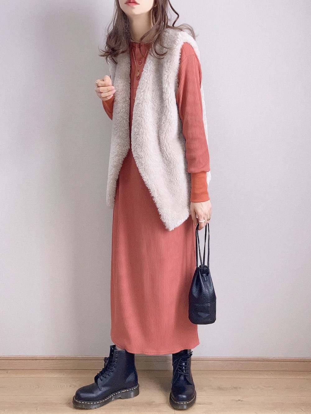 オレンジ系のワンピース、グレー系のベスト、ブラック系のブーツを着用したレディースの冬コーディネートの3枚目の写真