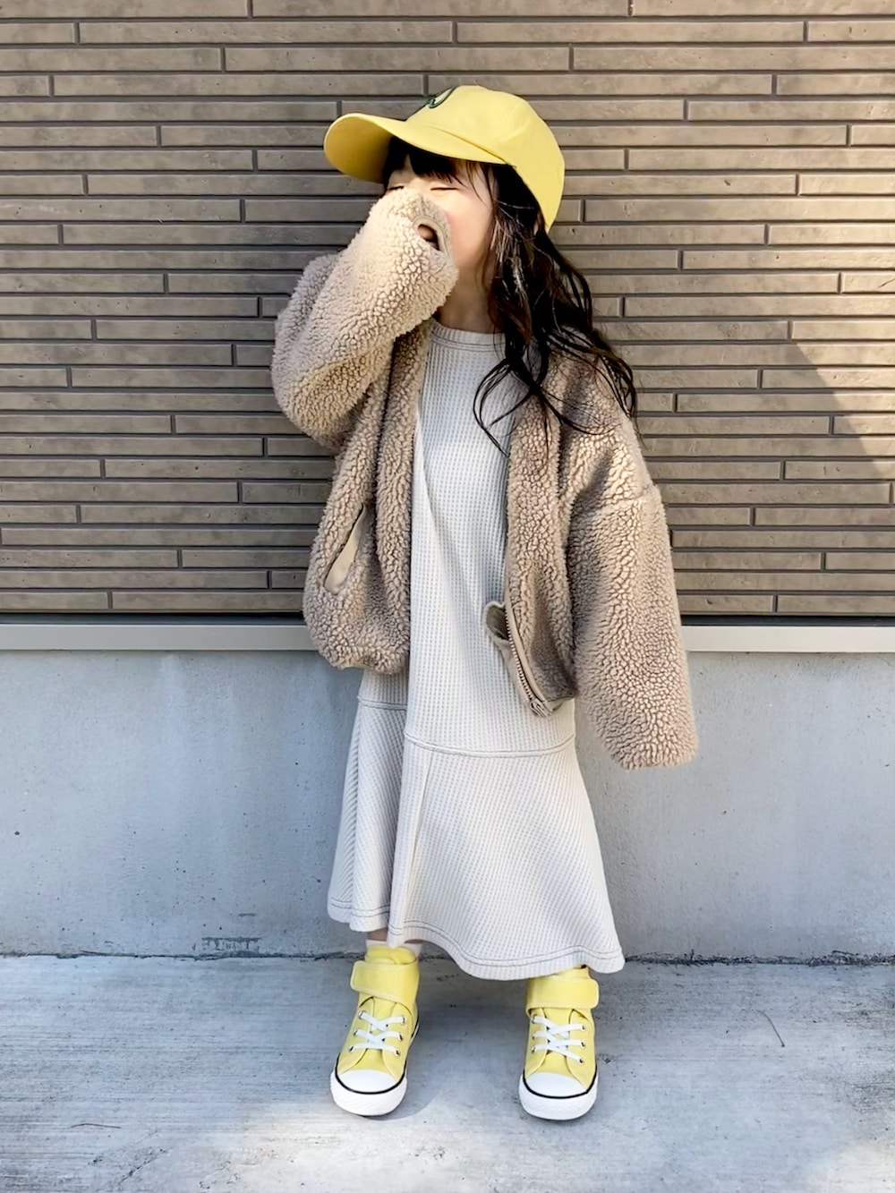 ベージュ系のワンピース、イエロー系のスニーカー、イエロー系のキャップを着用したキッズの冬コーディネートの3枚目の写真