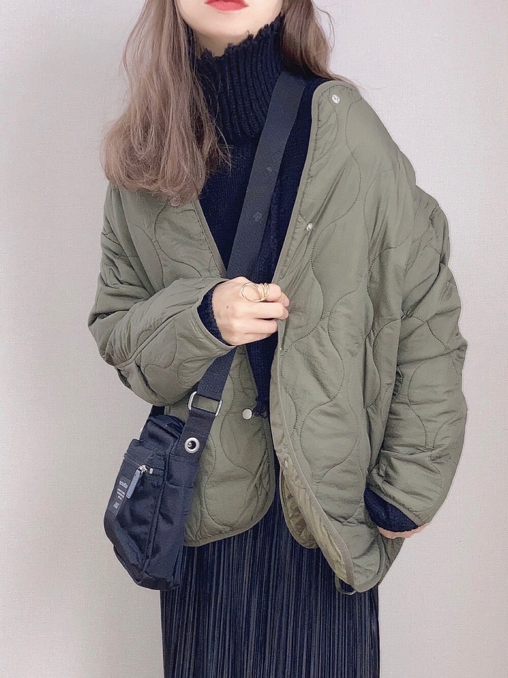 グリーン系のノーカラーコート、ブラック系のニット/セーター、ブラック系のスカートを着用したレディースの秋コーディネートの2枚目の写真