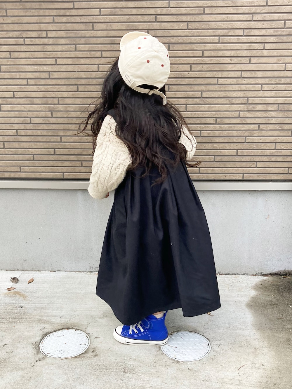 ブラック系のジャンパースカート、ホワイト系のニット/セーター、ブルー系のスニーカーを着用したキッズの冬コーディネートの4枚目の写真