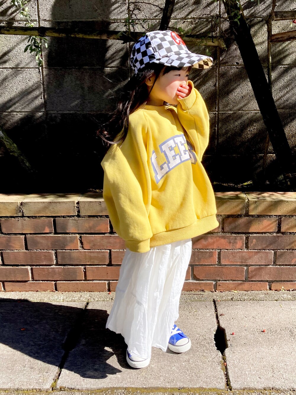 イエロー系のスウェット、ホワイト系のスカート、ブルー系のスニーカーを着用したキッズの冬コーディネートの2枚目の写真