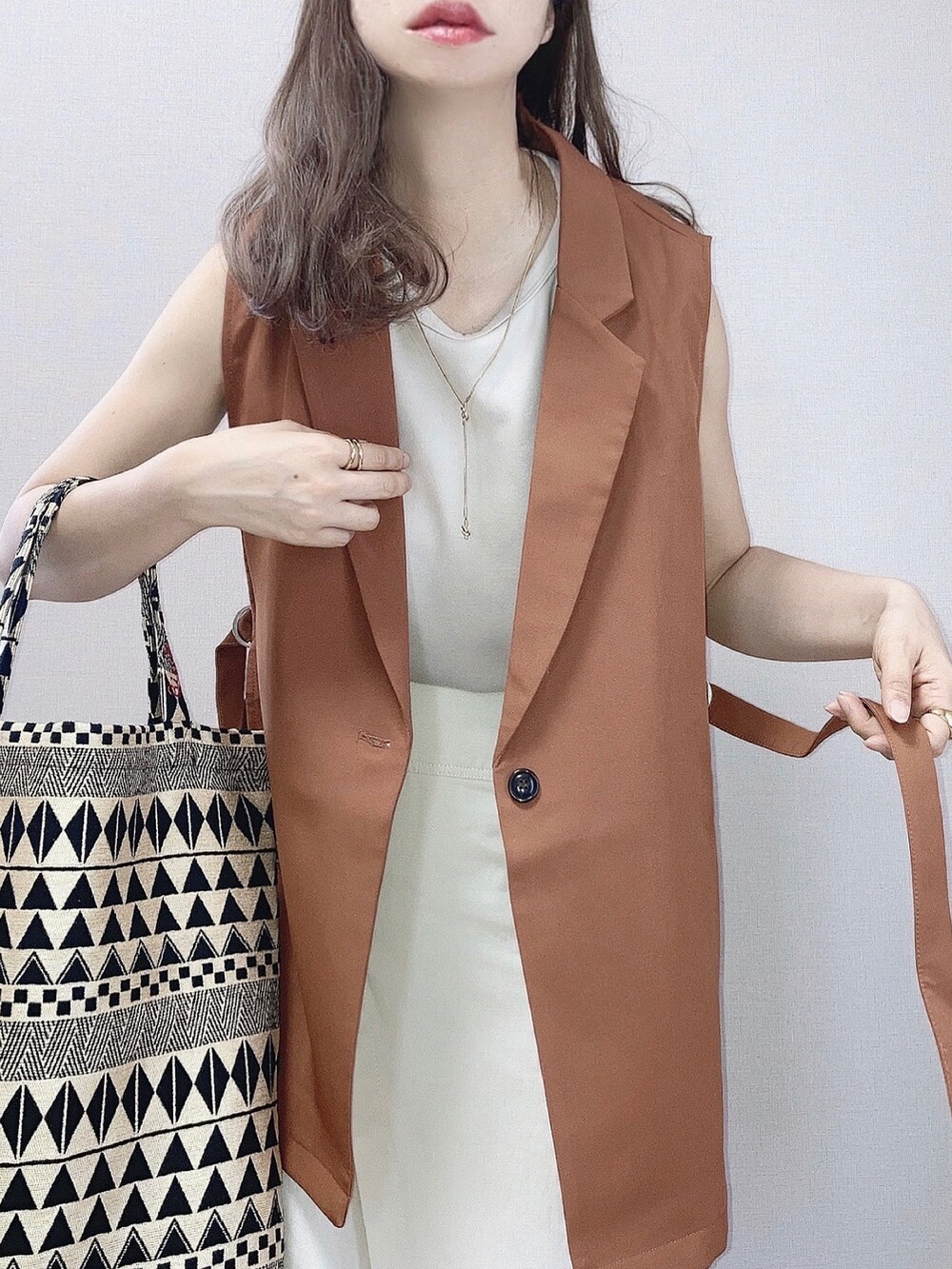 ブラウン系のベスト、ホワイト系のスカート、ブラック系のショルダーバッグを着用したレディースの夏コーディネートの2枚目の写真