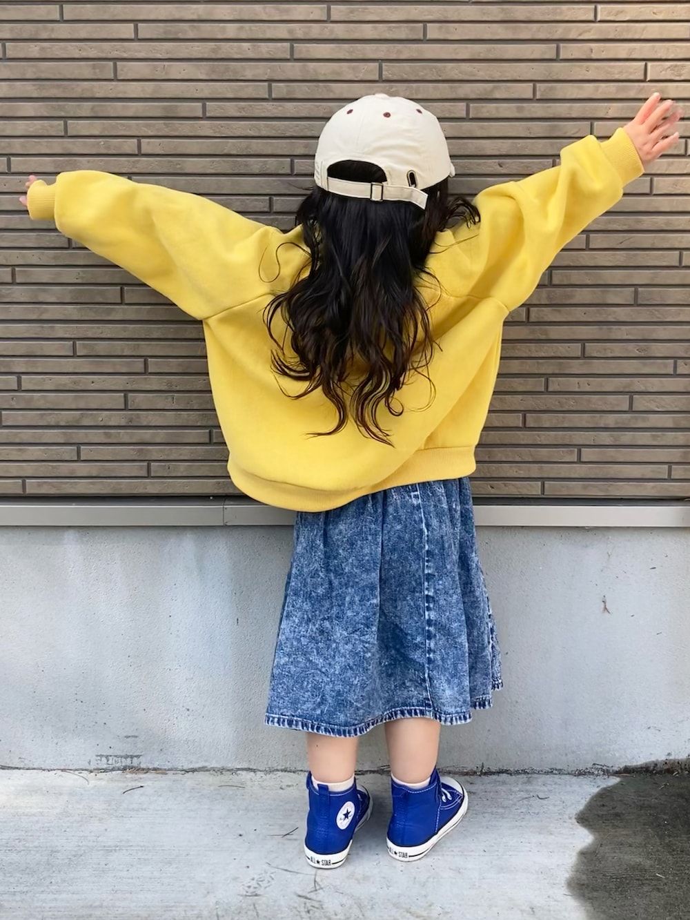 イエロー系のスウェット、ブルー系のデニムスカート、ブルー系のスニーカーを着用したキッズの春コーディネートの3枚目の写真