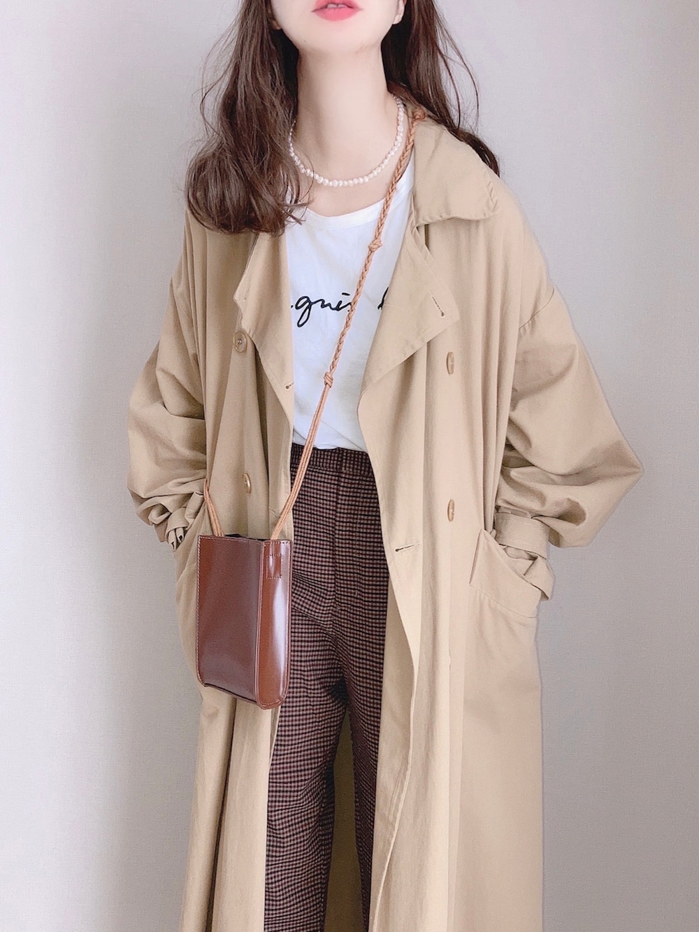 ベージュ系のトレンチコート、ホワイト系のTシャツ/カットソー、ブラウン系のパンツを着用したレディースの秋コーディネートの3枚目の写真