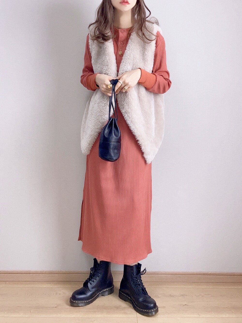 オレンジ系のワンピース、グレー系のベスト、ブラック系のブーツを着用したレディースの冬コーディネートの2枚目の写真