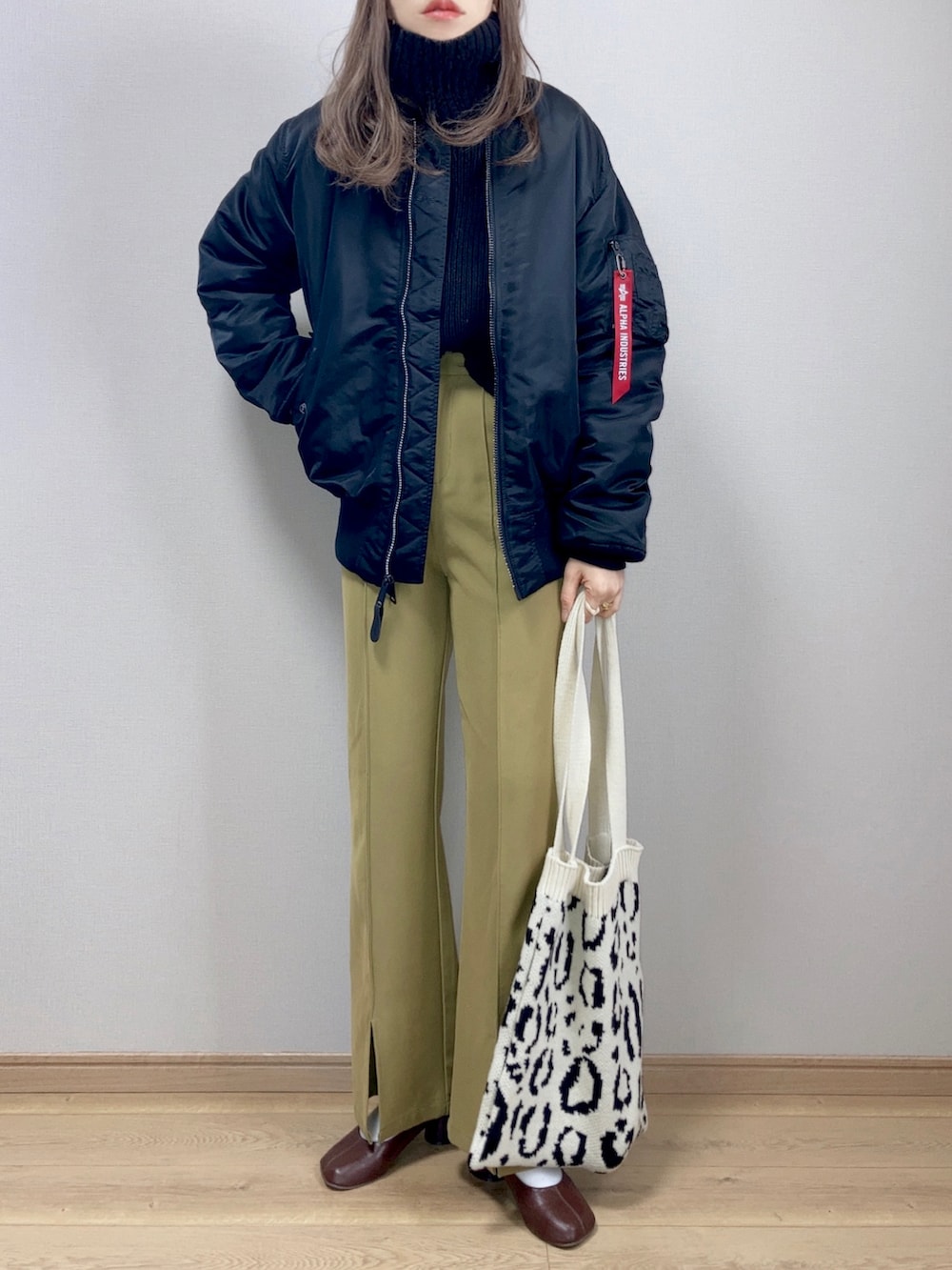 ブラック系のMA-1、グリーン系のスラックス、ホワイト系のトートバッグを着用したレディースの冬コーディネートの2枚目の写真