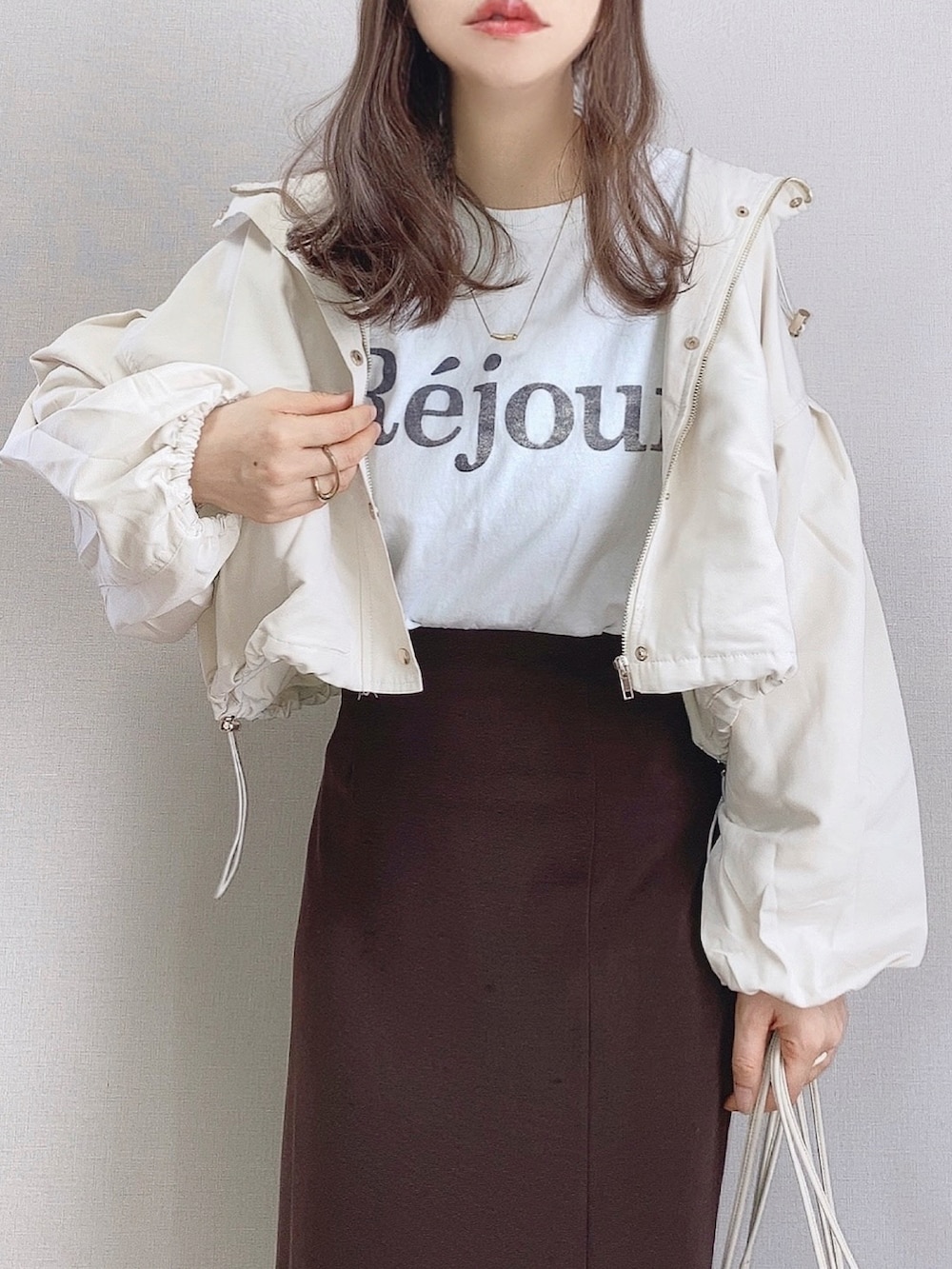 ホワイト系のマウンテンパーカー、ホワイト系のTシャツ/カットソー、ブラウン系のスカートを着用したレディースの春コーディネートの2枚目の写真