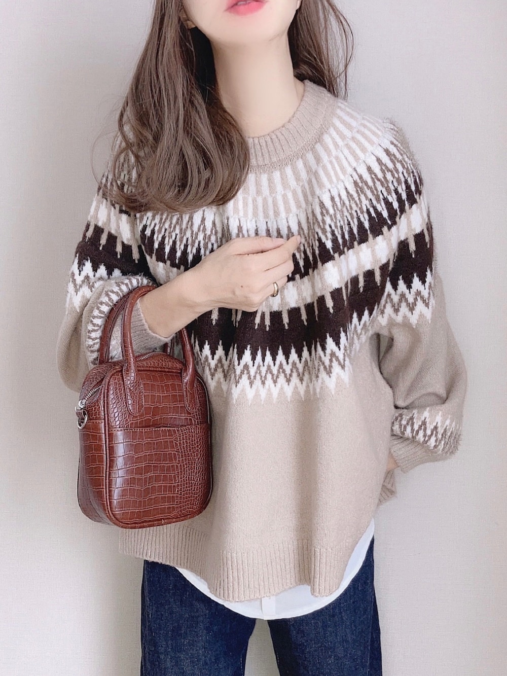 ベージュ系のニット/セーター、ブルー系のデニムパンツ、ブラウン系のハンドバッグを着用したレディースの秋コーディネートの2枚目の写真