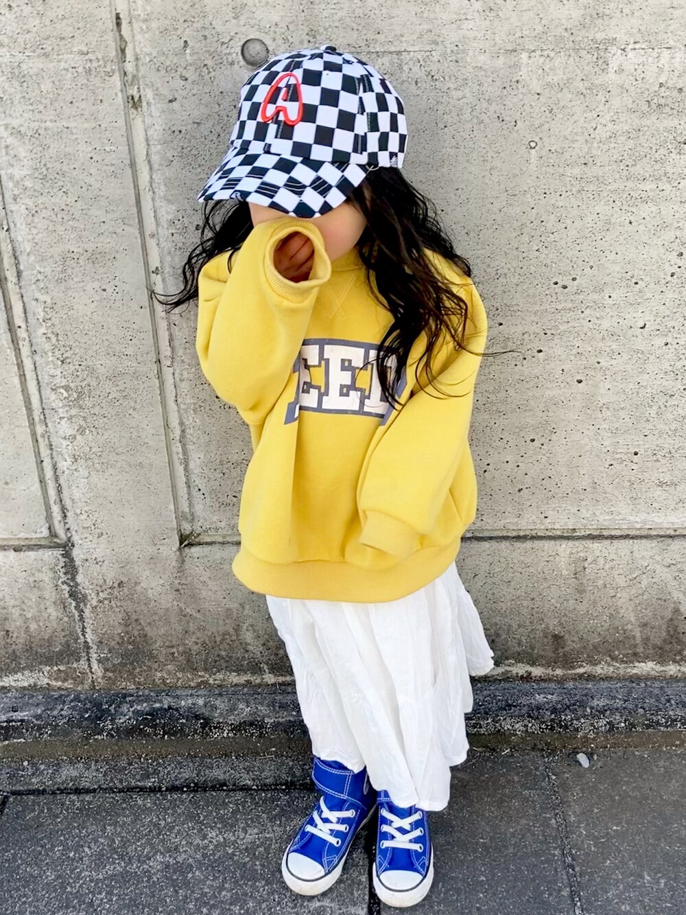 イエロー系のスウェット、ホワイト系のスカート、ブルー系のスニーカーを着用したキッズの冬コーディネートの3枚目の写真