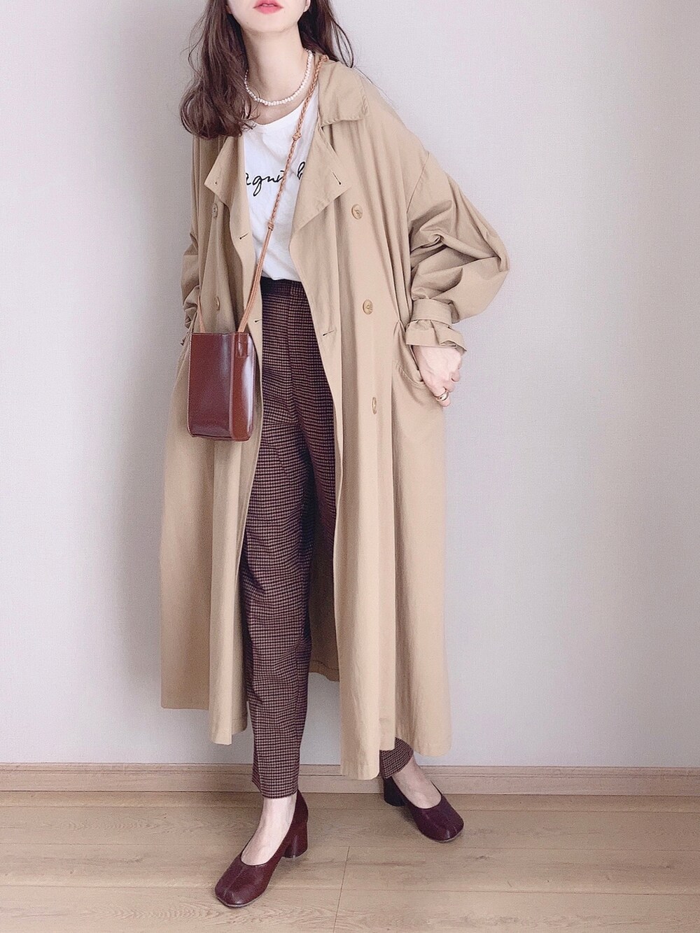 ベージュ系のトレンチコート、ホワイト系のTシャツ/カットソー、ブラウン系のパンツを着用したレディースの秋コーディネートの2枚目の写真