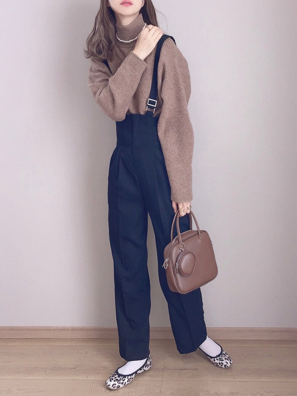 ブラウン系のノーカラーコート、ブラウン系のニット/セーター、ブラック系のサロペット/オーバーオールを着用したレディースの秋コーディネートの3枚目の写真