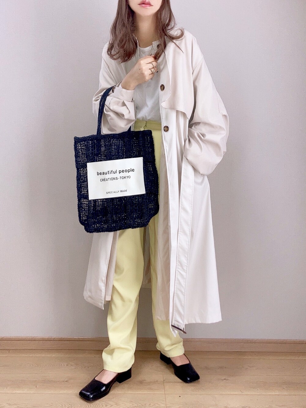 ベージュ系のステンカラーコート、ホワイト系のTシャツ/カットソー、イエロー系のスラックスを着用したレディースの春コーディネートの2枚目の写真