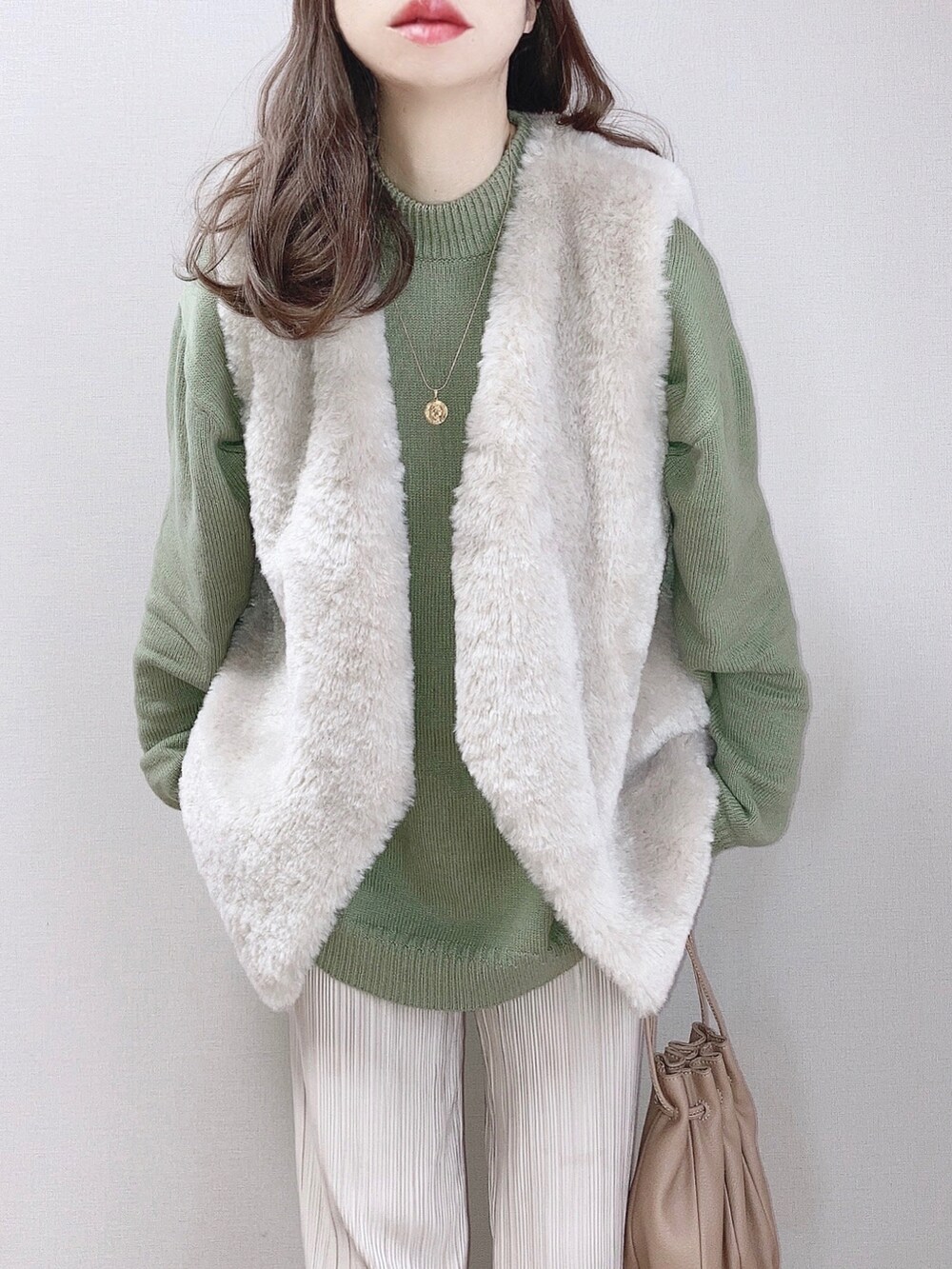 グリーン系のニット/セーター、グレー系のベスト、ベージュ系のスニーカーを着用したレディースの冬コーディネートの2枚目の写真