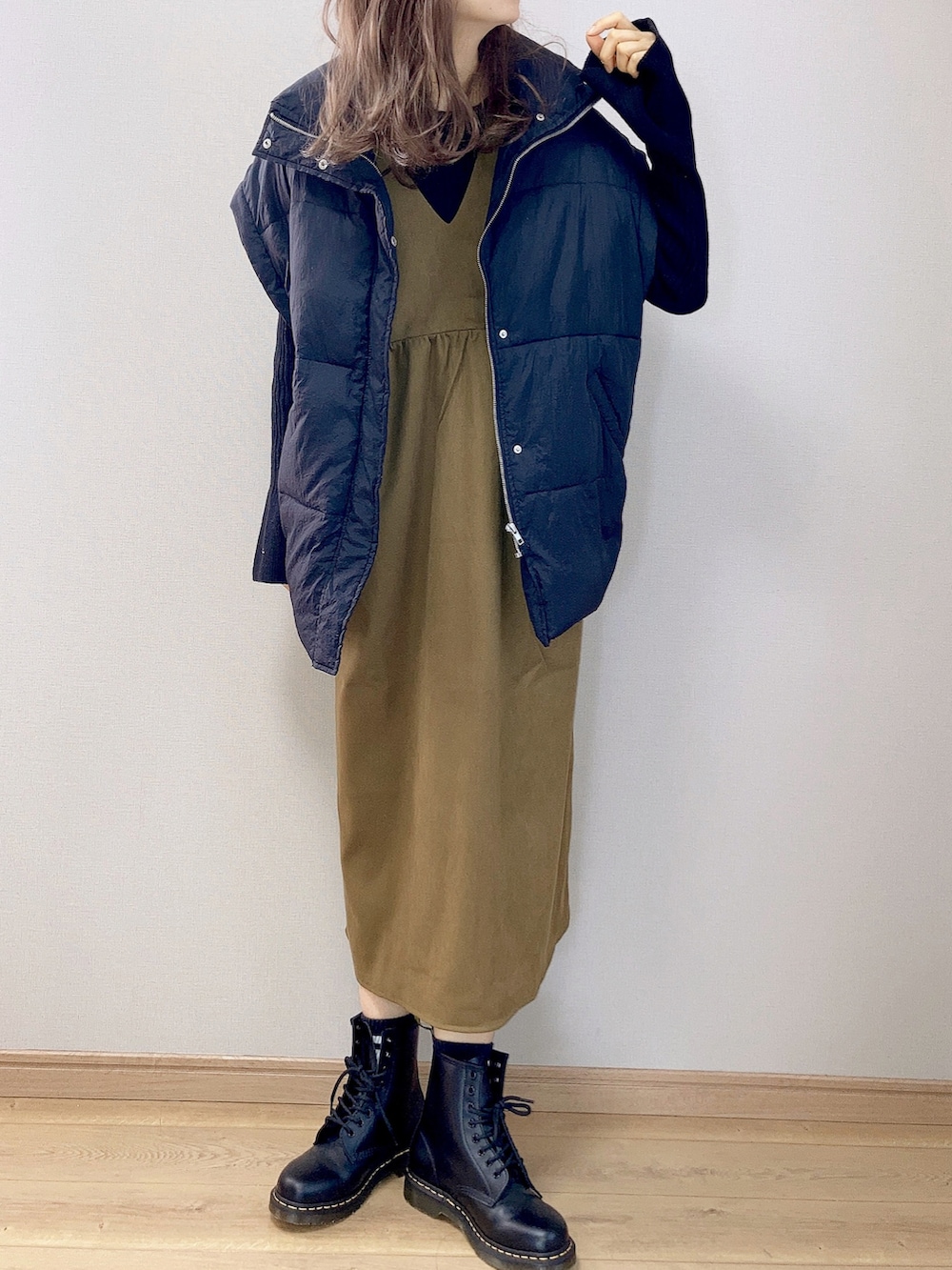 グリーン系のジャンパースカート、ブラック系のダウンベスト、ブラック系のブーツを着用したレディースの冬コーディネートの2枚目の写真