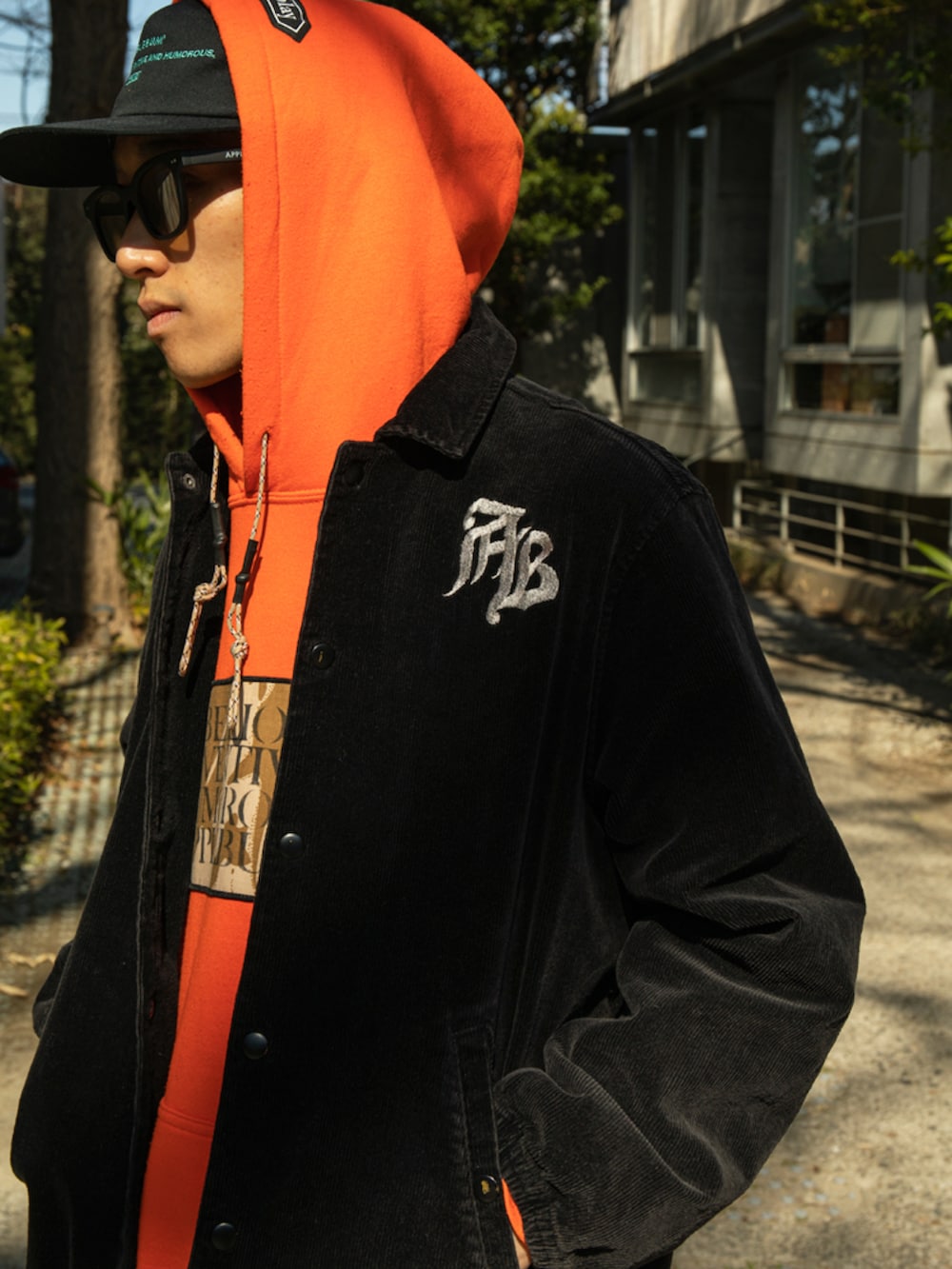 オレンジ系のパーカー、ブラック系のその他アウター、ブラック系のキャップを着用したメンズの冬コーディネートの2枚目の写真