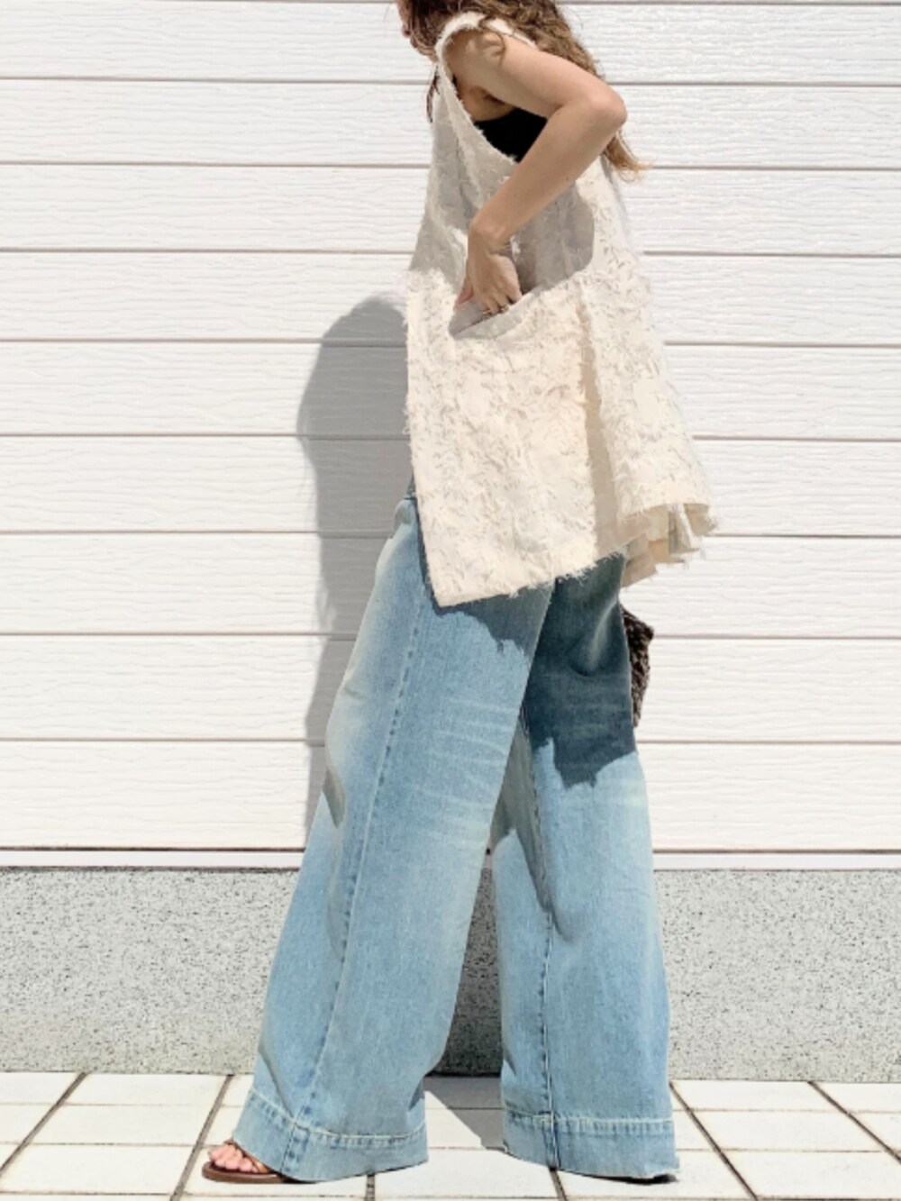 ブラウン系のクラッチバッグ、ブルー系のデニムパンツ、ブラック系のキャミソールを着用したレディースの夏コーディネートの2枚目の写真