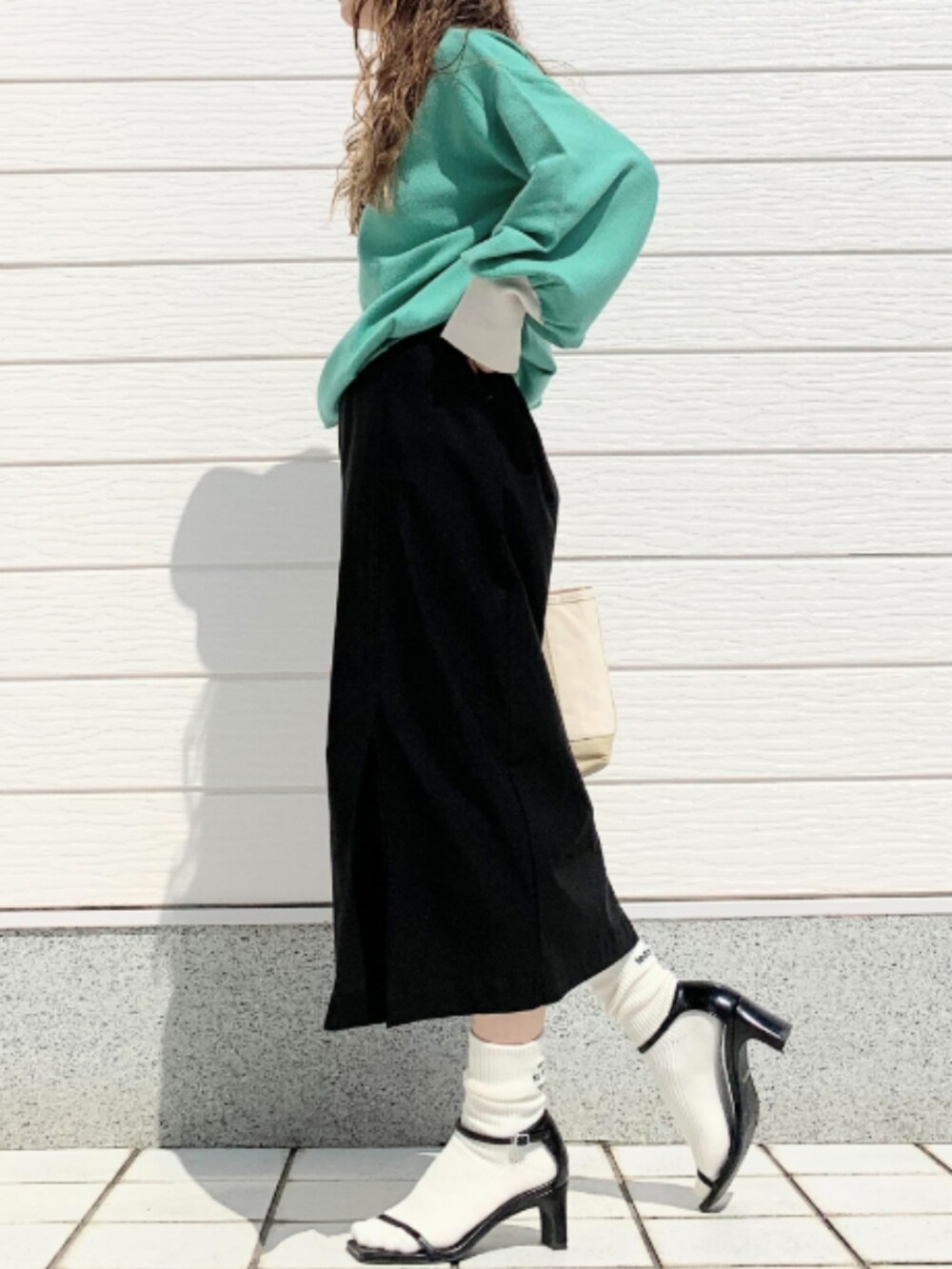 ベージュ系のトートバッグ、ブラック系のスカート、グリーン系のニット/セーターを着用したレディースの夏コーディネートの2枚目の写真