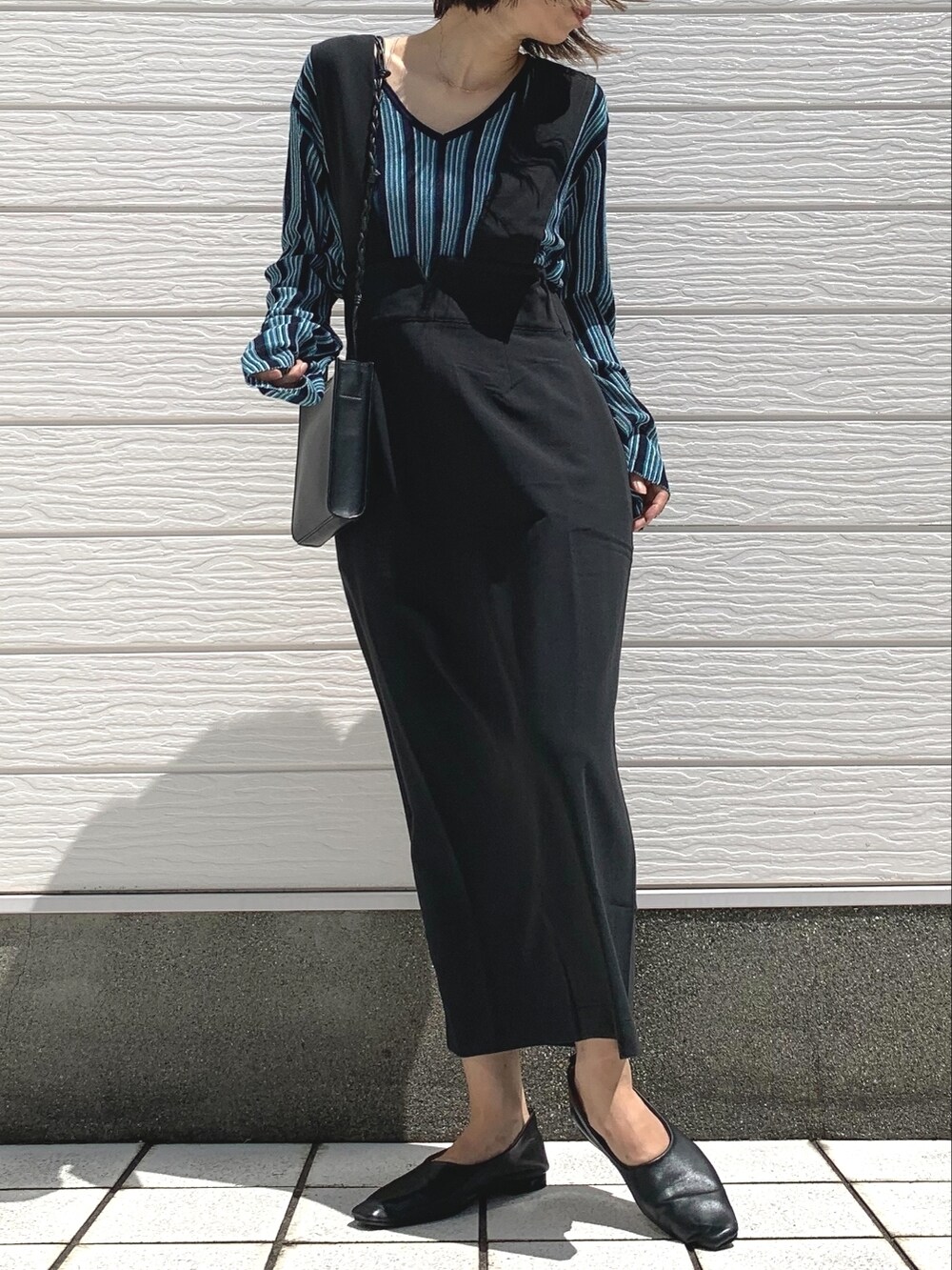 ブラック系のショルダーバッグ、ブルー系のニット/セーター、ブラック系のジャンパースカートを着用したレディースの夏コーディネートの2枚目の写真