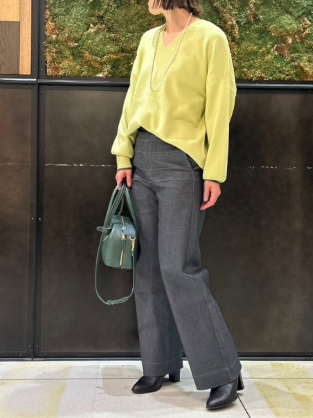グレー系のデニムパンツ、グリーン系のニット/セーター、グリーン系のボストンバッグを着用したレディースの秋コーディネートの3枚目の写真