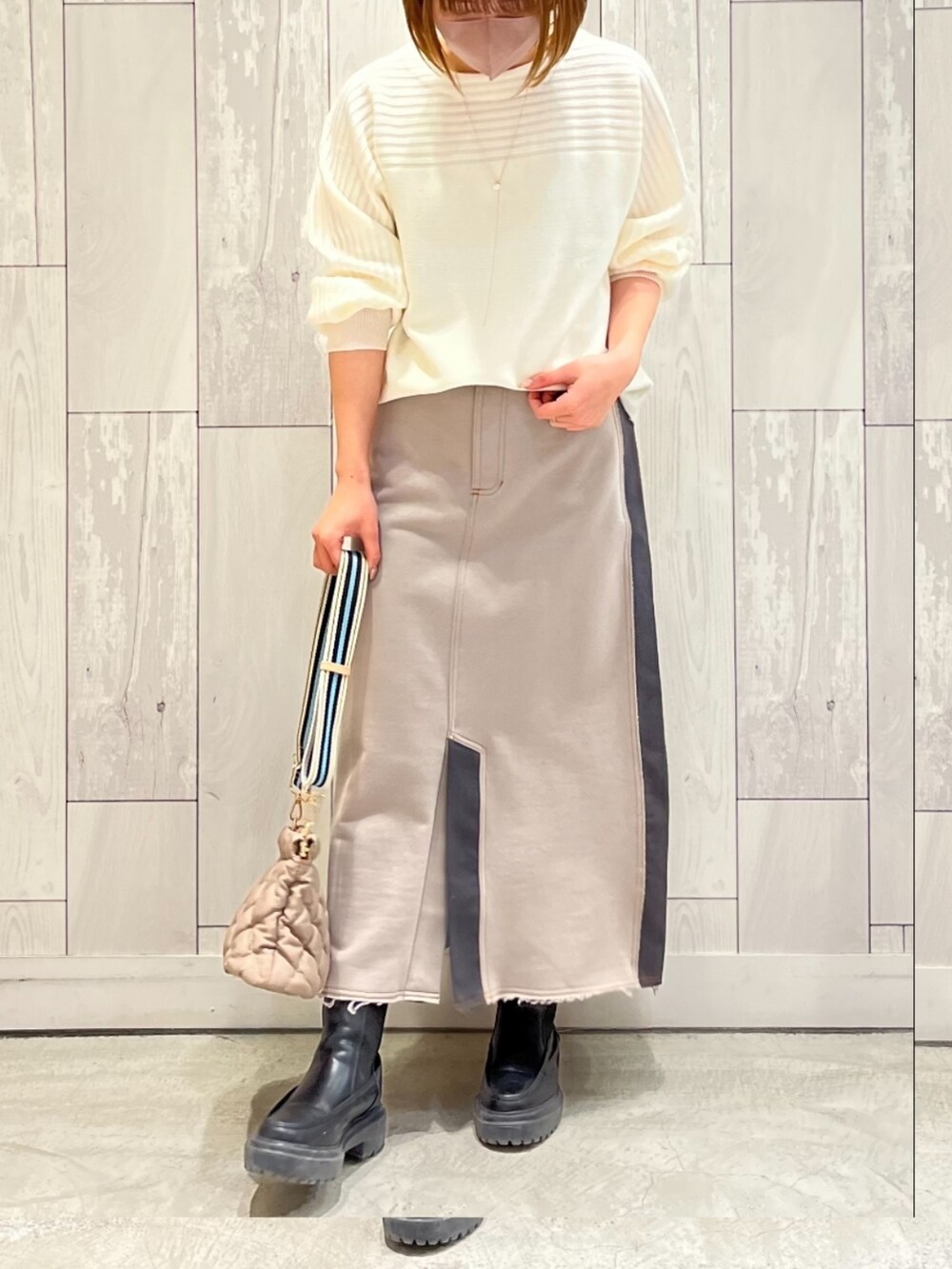 ベージュ系のショルダーバッグ、ベージュ系のスカート、ホワイト系のニット/セーターを着用したレディースの冬コーディネートの2枚目の写真