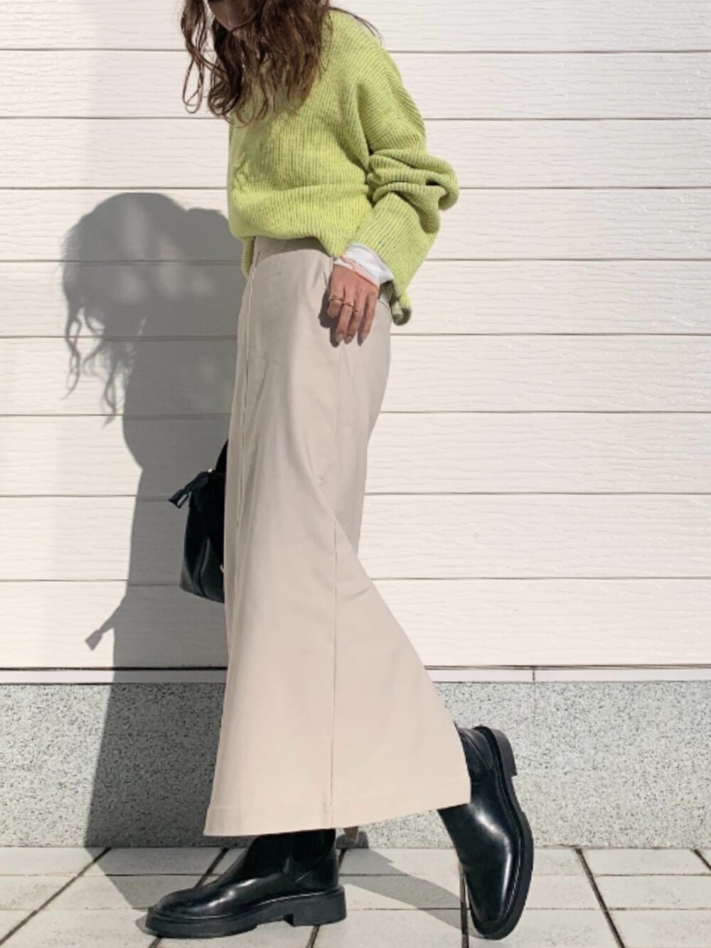 グレー系のニット/セーター、ホワイト系のスカート、ブラック系のトートバッグを着用したレディースの秋コーディネートの2枚目の写真