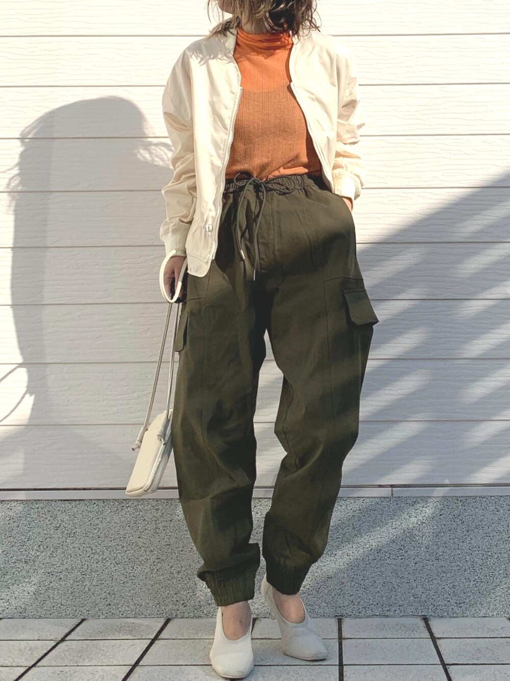グリーン系のその他パンツ、ホワイト系のショルダーバッグ、オレンジ系のTシャツ/カットソーを着用したレディースの冬コーディネートの2枚目の写真