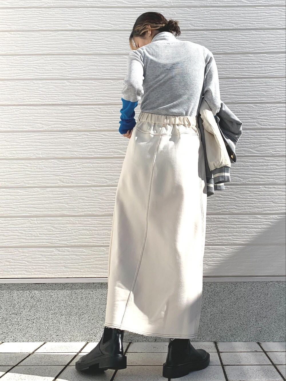 グレー系のスタジャン、ホワイト系のスカート、グレー系のニット/セーターを着用したレディースの秋コーディネートの4枚目の写真