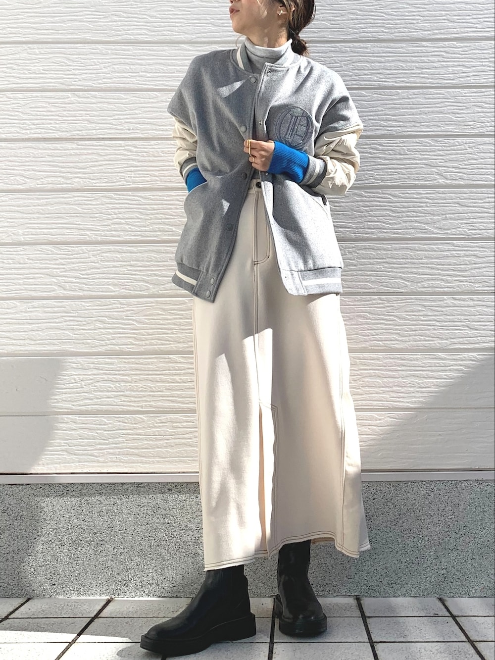 グレー系のスタジャン、ホワイト系のスカート、グレー系のニット/セーターを着用したレディースの秋コーディネートの2枚目の写真