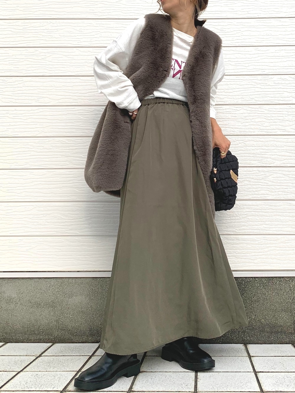 ブラック系のショルダーバッグ、グリーン系のスカート、ブラウン系のベストを着用したレディースの秋コーディネートの2枚目の写真