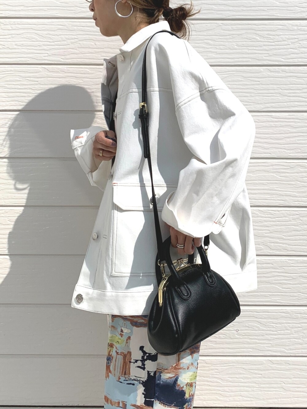 ブラック系のニット/セーター、ホワイト系のデニムジャケット、ブラック系のサンダルを着用したレディースの春コーディネートの4枚目の写真