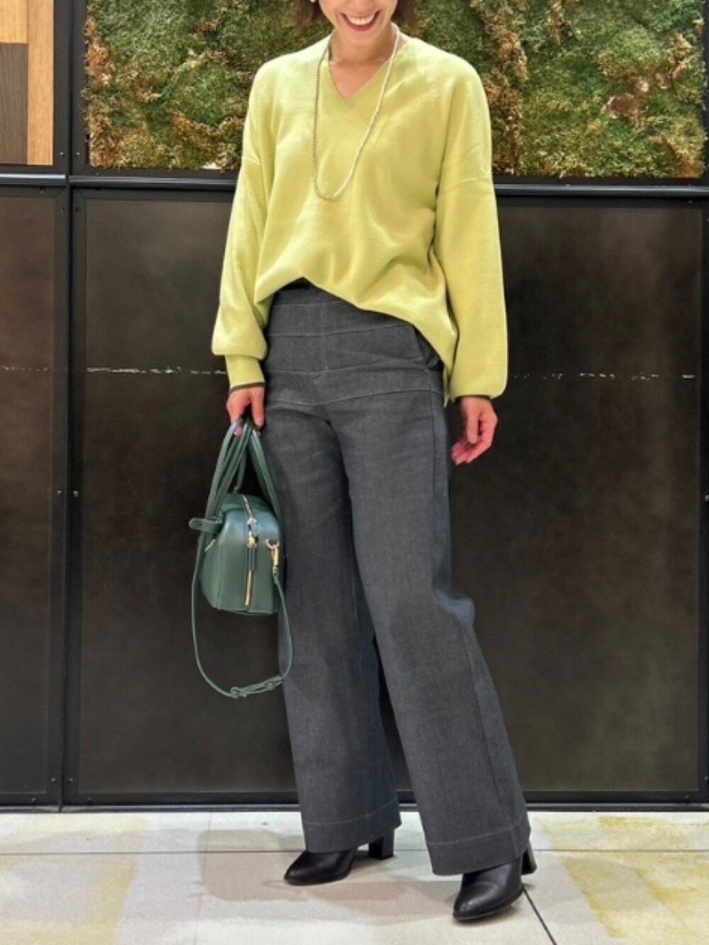 グレー系のデニムパンツ、グリーン系のニット/セーター、グリーン系のボストンバッグを着用したレディースの秋コーディネートの2枚目の写真