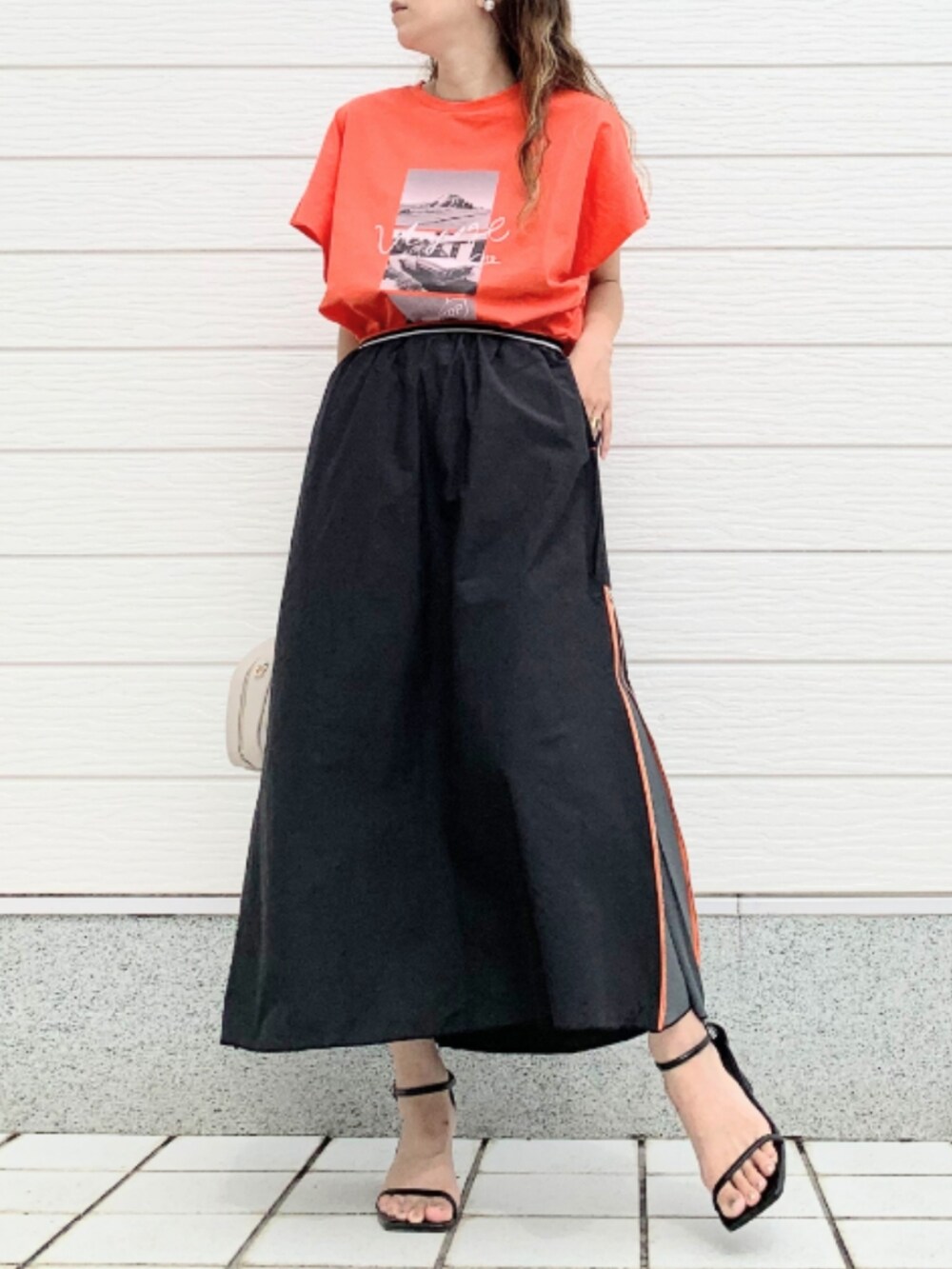 ブラック系のスカート、ホワイト系のボストンバッグ、オレンジ系のTシャツ/カットソーを着用したレディースの夏コーディネートの2枚目の写真