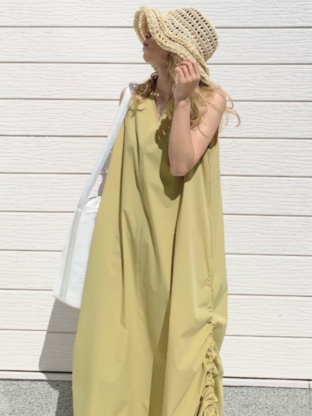 ブルー系のデニムパンツ、イエロー系のワンピース、ホワイト系のショルダーバッグを着用したレディースの春コーディネートの4枚目の写真