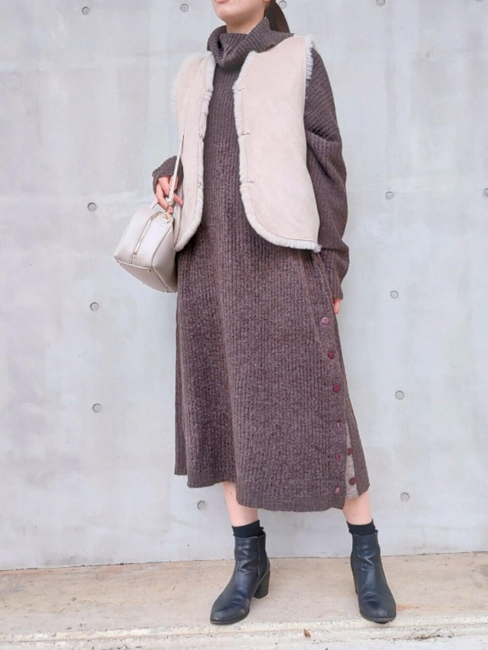 ホワイト系のボストンバッグ、ベージュ系のベスト、ブラウン系のワンピースを着用したレディースの秋コーディネートの2枚目の写真