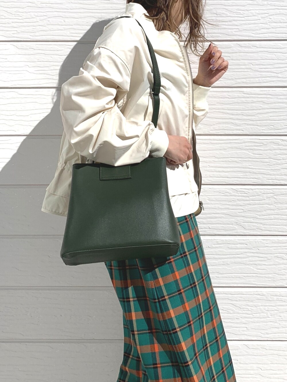 グリーン系のハンドバッグ、グリーン系のスカート、ベージュ系のブルゾンを着用したレディースの春コーディネートの3枚目の写真