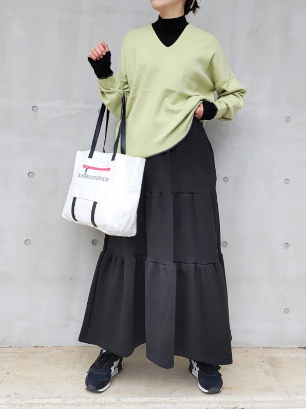 ブラック系のスカート、ブラック系のスニーカー、グリーン系のニット/セーターを着用したレディースの秋コーディネートの2枚目の写真