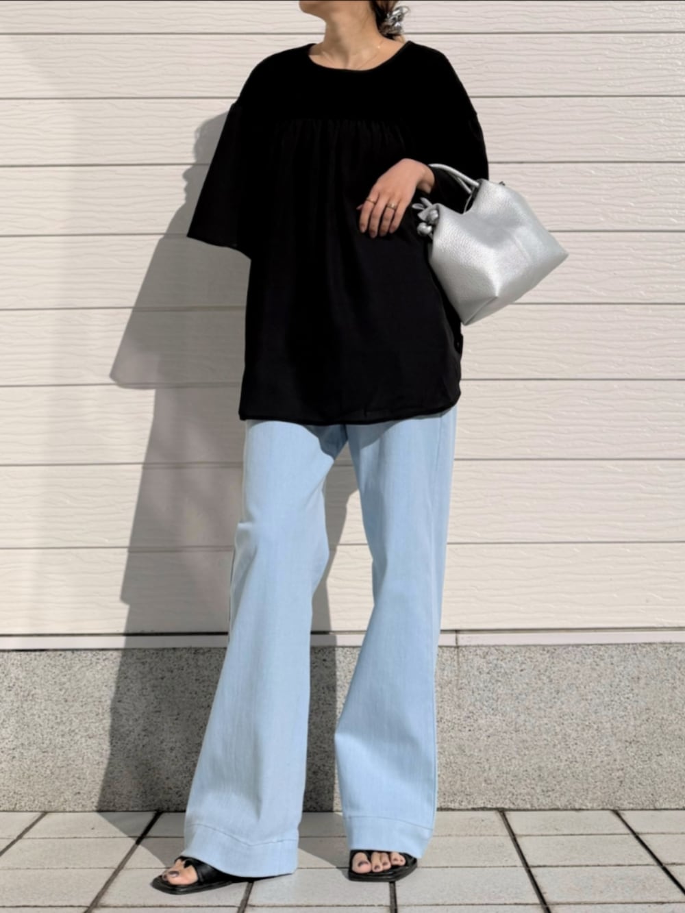 ブルー系のデニムパンツ、シルバー系のトートバッグ、ブラック系のシャツ/ブラウスを着用したレディースの春コーディネートの2枚目の写真
