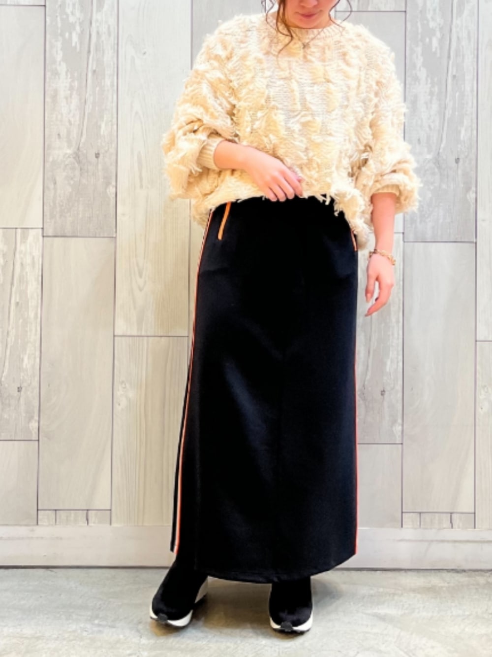 ブラック系のスカート、ホワイト系のニット/セーター、ブラック系のブーツを着用したレディースの秋コーディネートの2枚目の写真