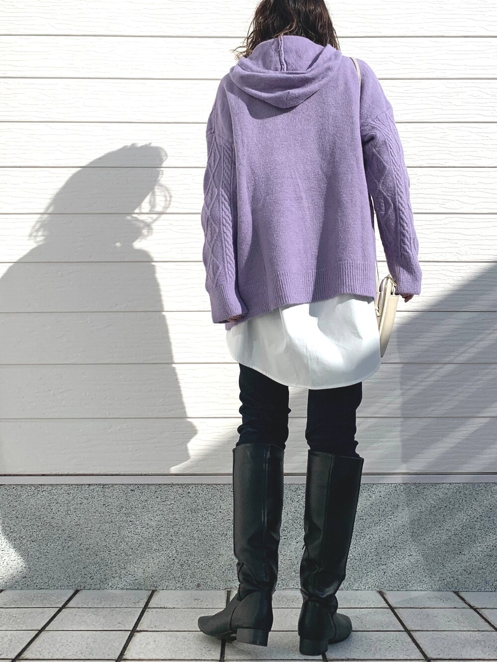 ブラック系のブーツ、ブルー系のデニムパンツ、ホワイト系のショルダーバッグを着用したレディースの秋コーディネートの3枚目の写真