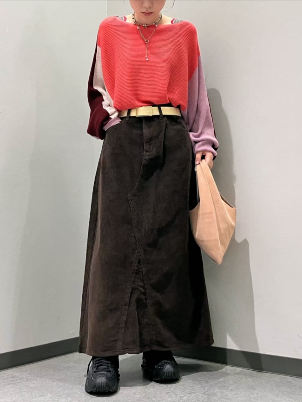 レッド系のニット/セーター、ブラウン系のスカート、ベージュ系のトートバッグを着用したレディースの秋コーディネートの2枚目の写真