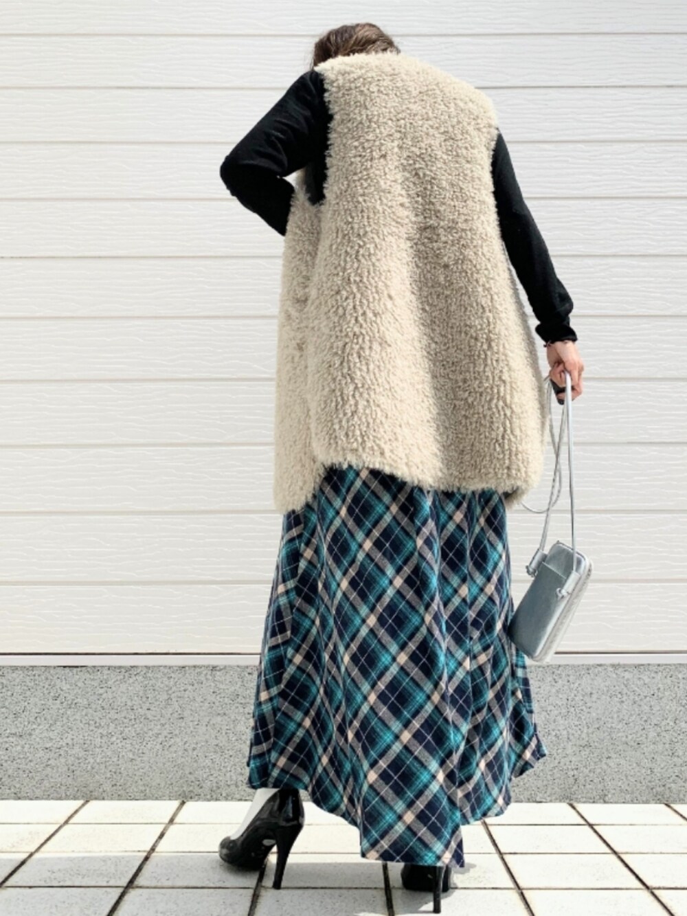 ベージュ系のベスト、シルバー系のショルダーバッグ、ブルー系のスカートを着用したレディースの秋コーディネートの2枚目の写真