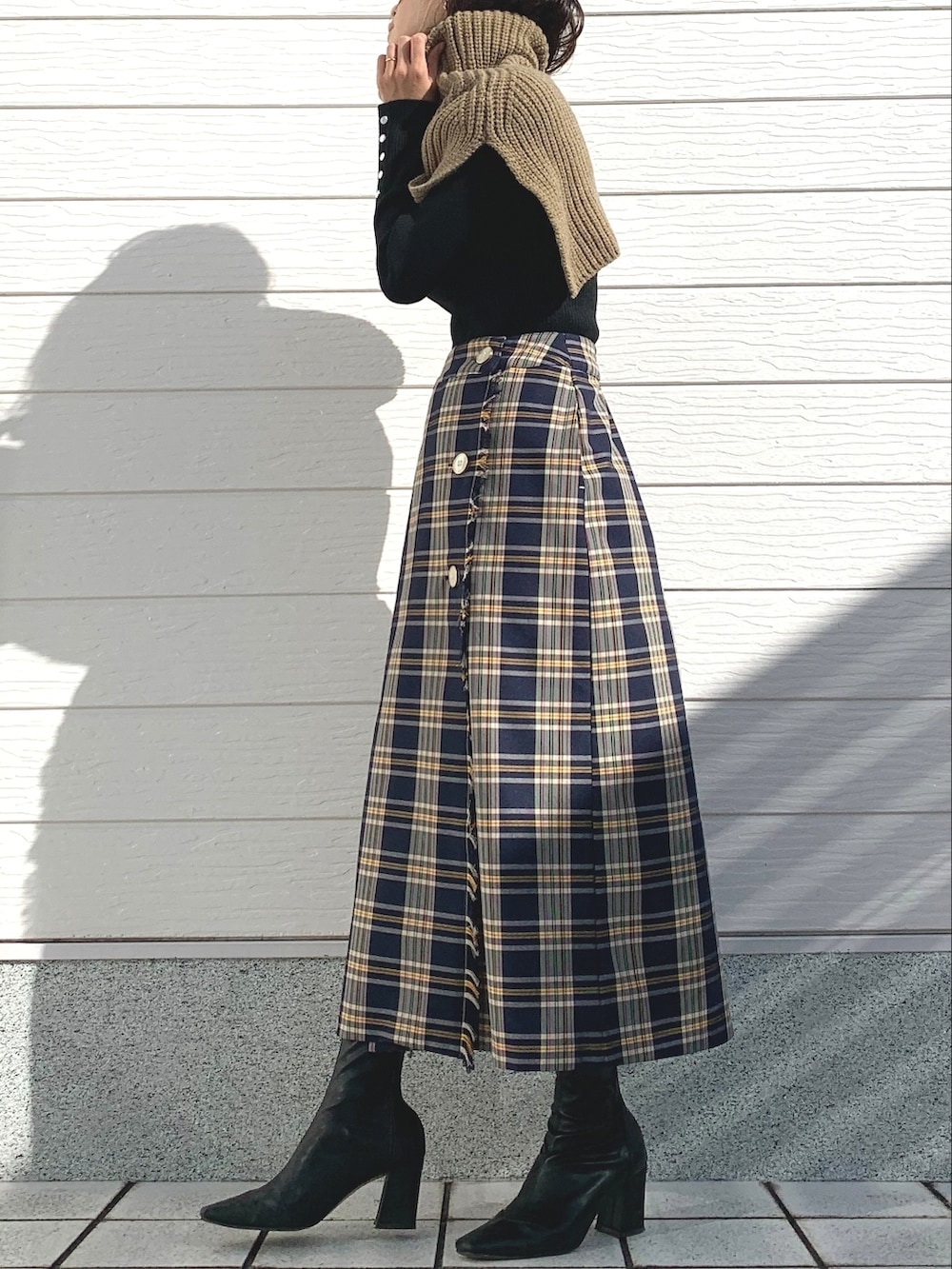 ブルー系のスカート、ブラック系のニット/セーター、ベージュ系のネックウォーマー/スヌードを着用したレディースの秋コーディネートの2枚目の写真