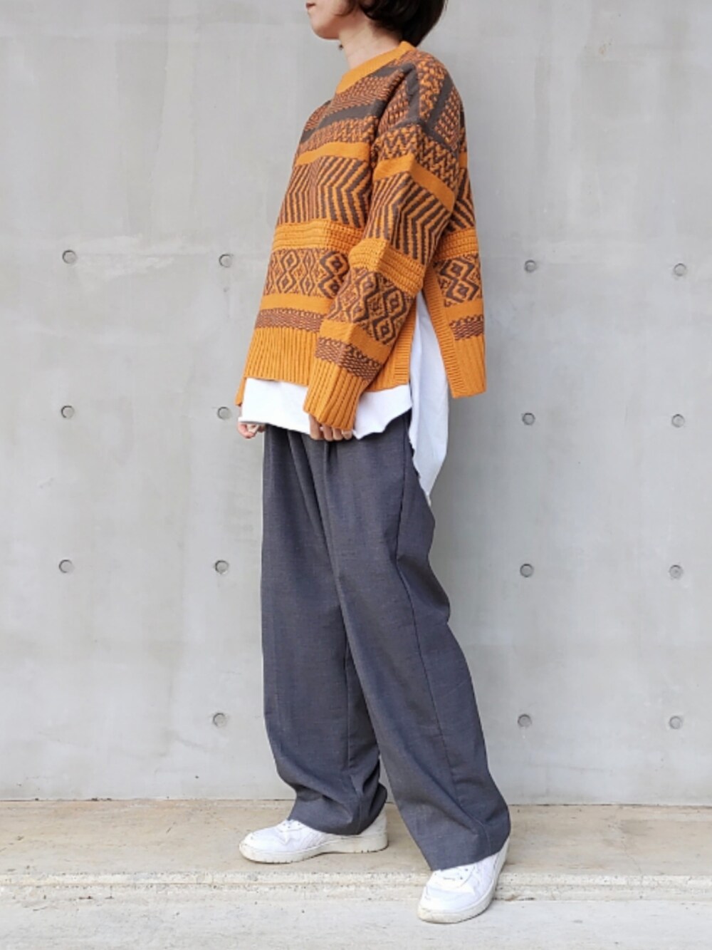 グレー系のスラックス、ホワイト系のTシャツ/カットソー、イエロー系のニット/セーターを着用したレディースの秋コーディネートの2枚目の写真